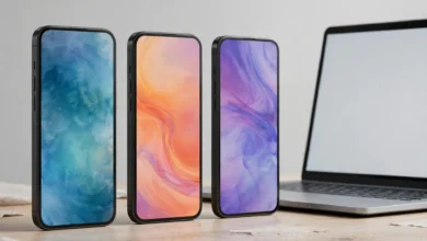 Three modern smartphones standing on a desk next to a laptop